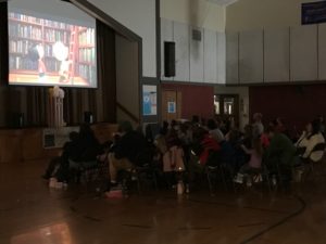 children and adults watching Charlie Brown movie in a gymnasium