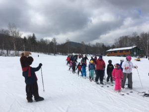 Monty Moose looking at long line of skiers waiting for the ski lift