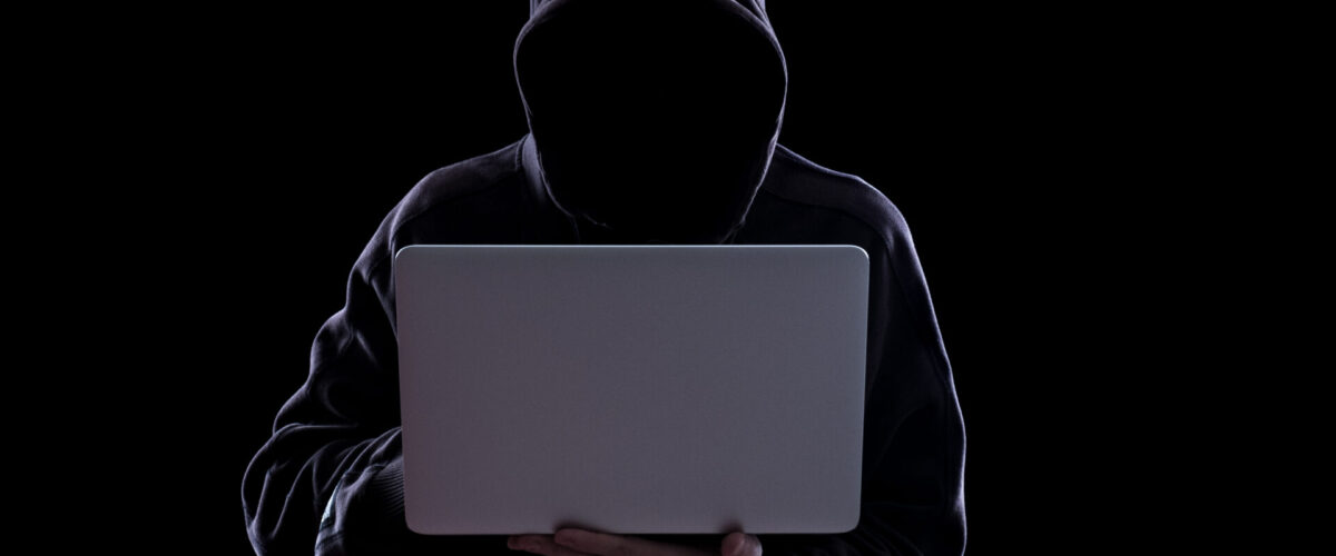 man with hood on in dark with laptop